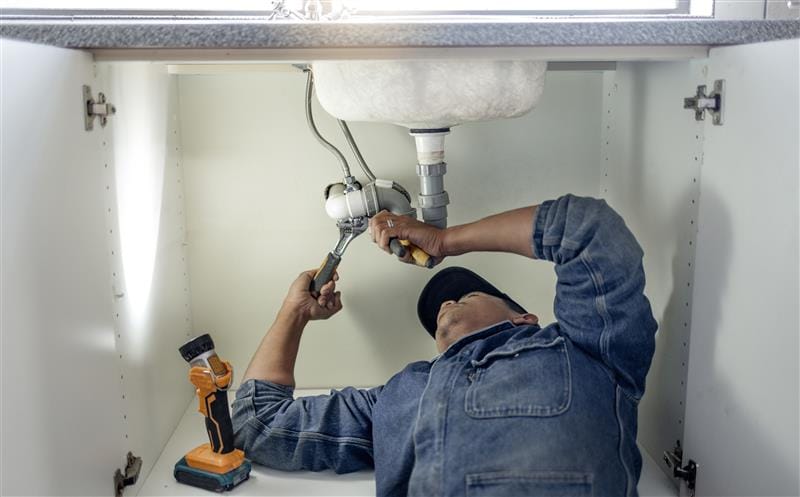 Plumber repairing pipes beneath a bathroom sink in Maitland