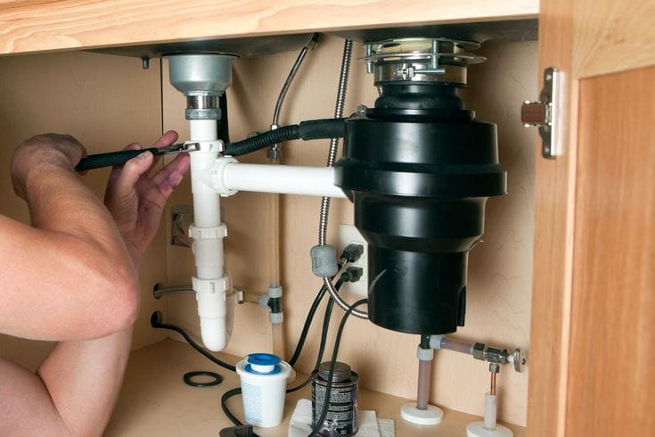 Plumber installing a garbage disposal beneath a kitchen sink in Maitland