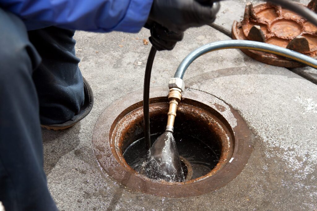 Plumber hydro jetting a sewer line through a manhole in Maitland