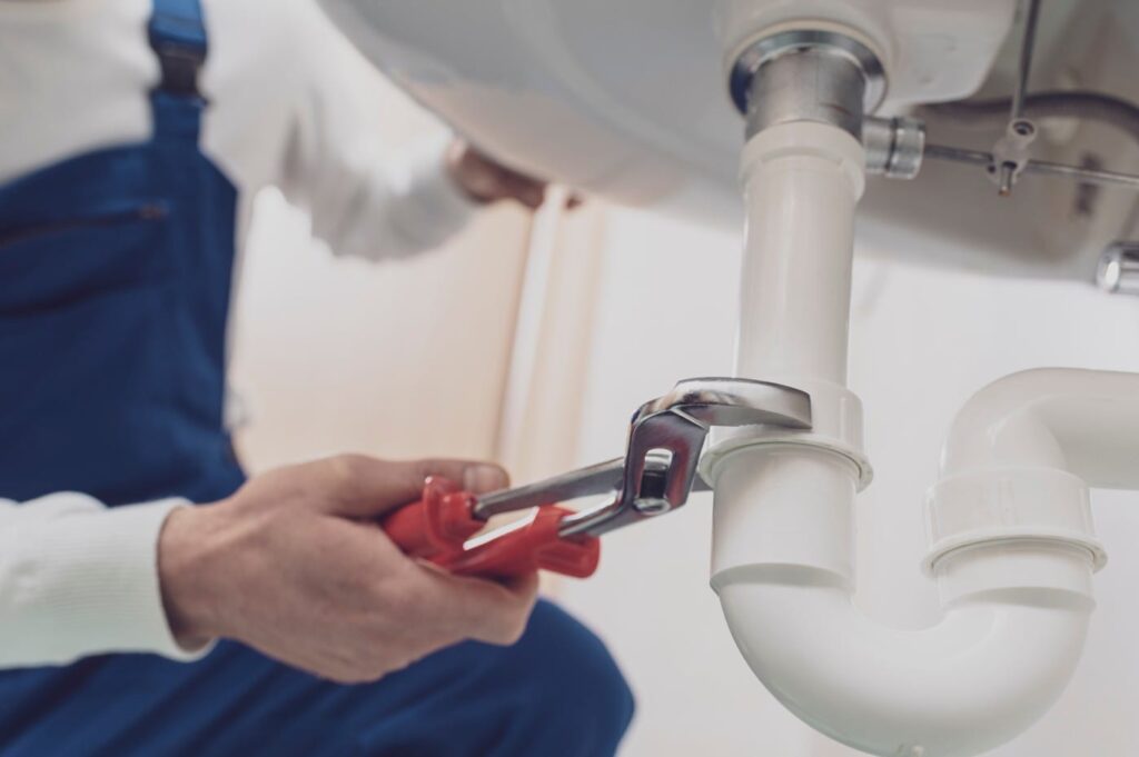 Plumber repairing a white drain pipe beneath a sink in Maitland