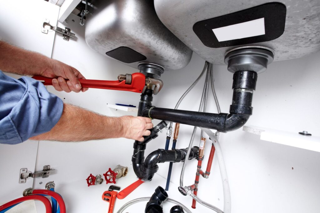 Plumber repairing drain pipes beneath a kitchen sink in Maitland